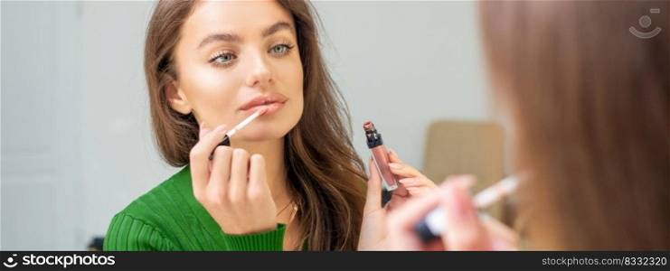 Beautiful young caucasian woman applying gloss to the lips looking in the mirror. Out of focus. Woman applying gloss to the lips