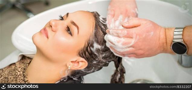 Beautiful young caucasian woman gets hair wash by male hands of hairdresser in hair salon. Young woman gets hair wash