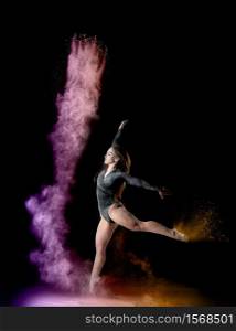 beautiful young caucasian woman in a black bodysuit with a sports figure dancing in a purple-yellow cloud of flour on a black background, explosion and expression in motion