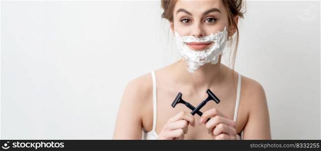Beautiful young caucasian woman with shaving foam on her face and two razors in her hands on white background. Woman with shaving foam on her face