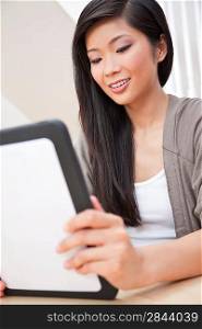 Beautiful young Chinese Asian woman at home using tablet computer and smiling
