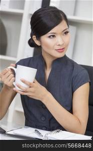 Beautiful young Chinese Asian woman businesswoman relaxing and drinking a cup of coffee or tea in her office