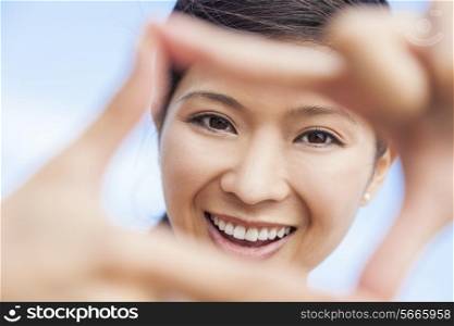 Beautiful young Chinese Asian woman girl smiling, making and looking through a finger frame