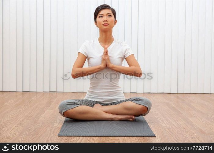 Beautiful young Chinese Asian woman sitting cross legged in a yoga position at a gym or health spa