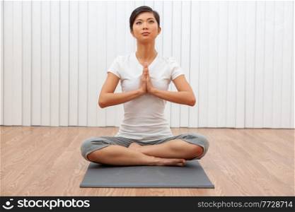 Beautiful young Chinese Asian woman sitting cross legged in a yoga position at a gym or health spa