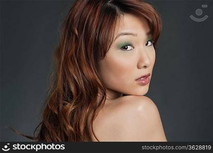 Beautiful young Chinese woman looking back over colored background