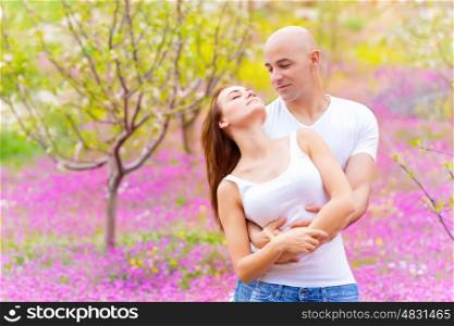 Beautiful young couple hugging in spring garden, tender pink flowers field, romantic and love concept