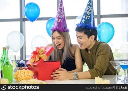 Beautiful young couple is celebrating at home. Handsome man is giving his girlfriend a gift box