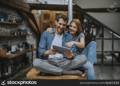 Beautiful young couple is using a digital tablet and smiling in kitchen at home