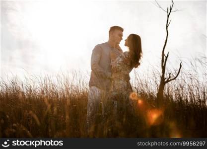 beautiful young couple kissing in a field with grass at sunset. stylish man and woman having fun outdoors. family day concept. copy space. beautiful young couple kissing in a field with grass at sunset. stylish man and woman having fun outdoors. family day concept. copy space.