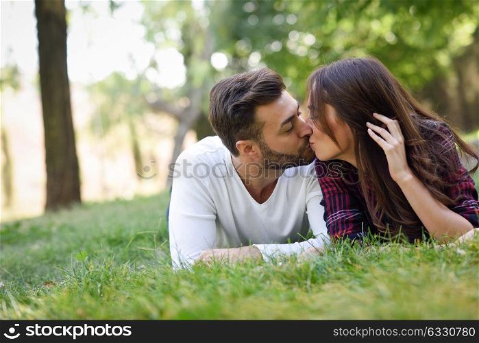 Beautiful young couple kissing on grass in an urban park. Caucasian man and woman wearing casual clothes.