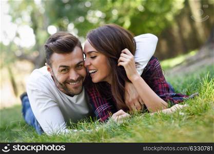 Beautiful young couple laying on grass in an urban park. Caucasian man and woman wearing casual clothes.