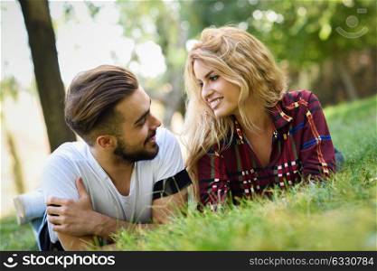 Beautiful young couple laying on grass in an urban park. Caucasian man and woman wearing casual clothes. Blonde female.