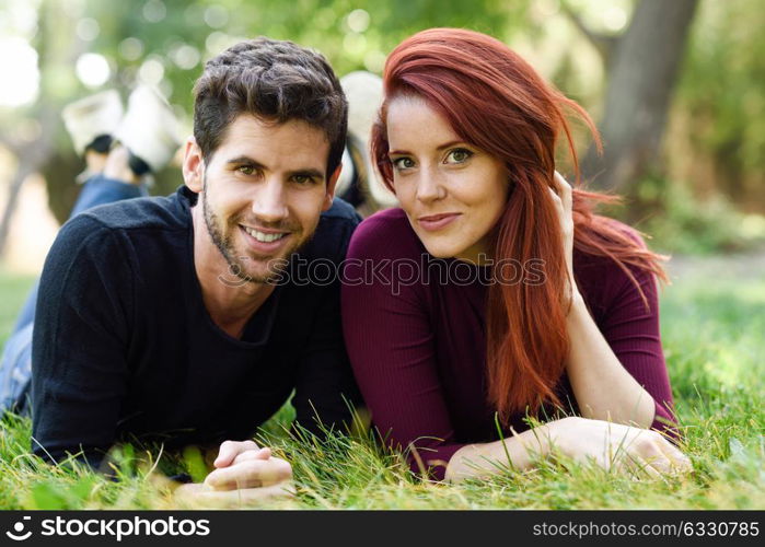 Beautiful young couple laying on grass in an urban park. Caucasian guy and girl wearing casual clothes. Redhead girl.