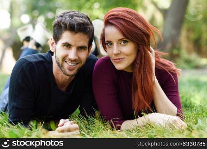 Beautiful young couple laying on grass in an urban park. Caucasian guy and girl wearing casual clothes. Redhead girl.