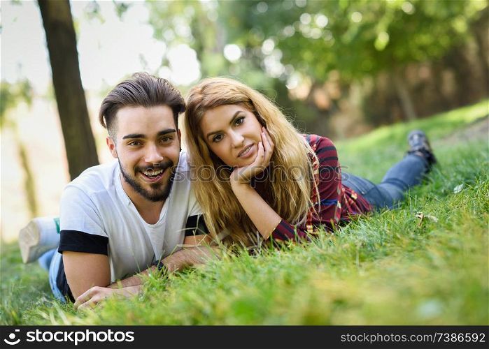 Beautiful young couple laying on grass in an urban park. Caucasian man and woman wearing casual clothes. Blonde female.. Beautiful young couple laying on grass in an urban park.