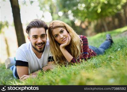 Beautiful young couple laying on grass in an urban park. Caucasian man and woman wearing casual clothes. Blonde female.. Beautiful young couple laying on grass in an urban park.