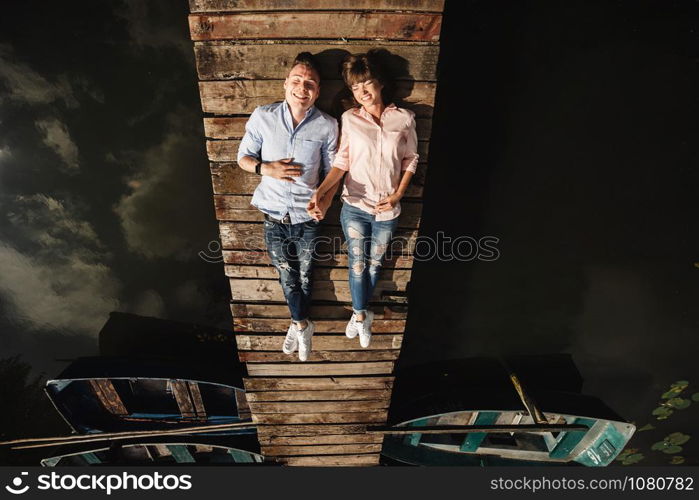 Beautiful young couple lies on a wooden bridge on the lake, looks lovingly at each other and smiles. Loving couple. Love story. Beautiful young couple lies on a wooden bridge on the lake, looks lovingly at each other and smiles. Love story.