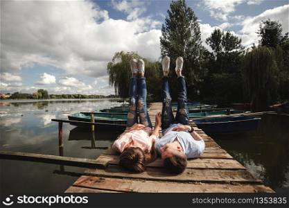 Beautiful young couple lies on a wooden bridge on the lake, looks lovingly at each other and smiles. Loving couple. Love story. Beautiful young couple lies on a wooden bridge on the lake, looks lovingly at each other and smiles. Love story.