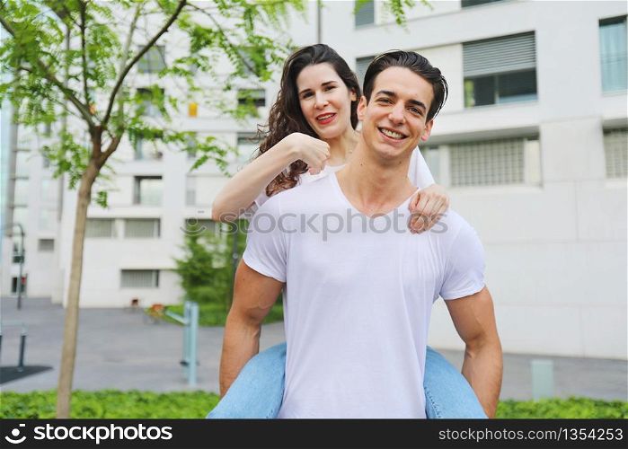 Beautiful young couple looking at camera and smiling while standing outdoors. Girl piggyback