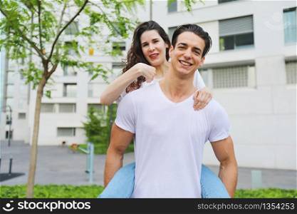 Beautiful young couple looking at camera and smiling while standing outdoors. Girl piggyback
