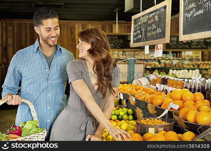 Beautiful young couple looking at each other while shopping in supermarket