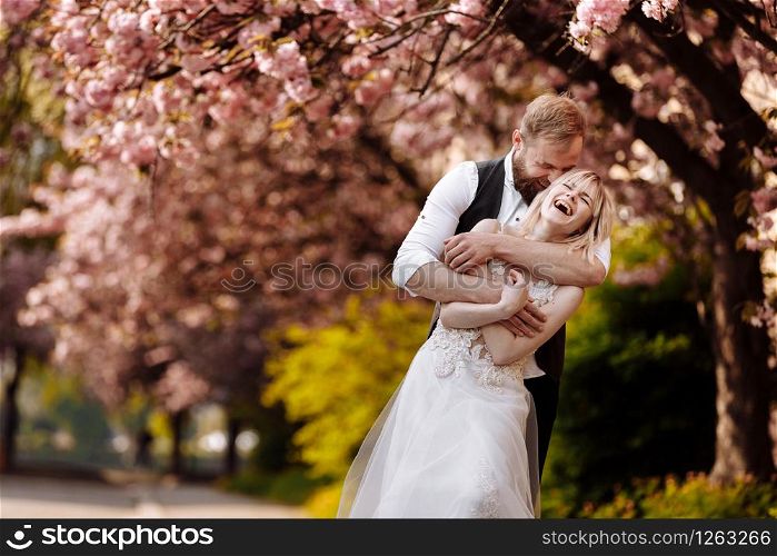 beautiful young couple, man with beard and blonde woman hugging in the spring park. Stylish couple near the tree with sakura. Concept spring. fashion and beauty.. beautiful young couple, man with beard and blonde woman hugging in the spring park. Stylish couple near the tree with sakura. Concept spring. fashion and beauty
