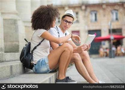 beautiful young couple of tourists sitting and looking at map