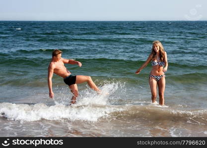 Beautiful young couple playing in the ocean splashing water, heaving fun on a summer day