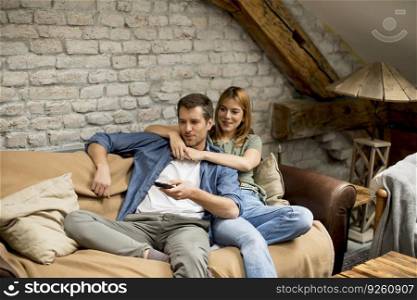 Beautiful young couple using remote control whi e watching TV at home