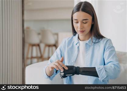 Beautiful young disabled girl with bionic prosthetic arm, learning to turn on her high tech prosthesis. Female with disability using robotic artificial limb. Medical technologies concept.. Beautiful young disabled girl with bionic prosthetic arm learning to turn on high tech prosthesis