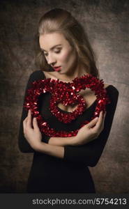 Beautiful, young, elegance, girl with brown nice long hairstyle and black top is holding heart symbol of love.