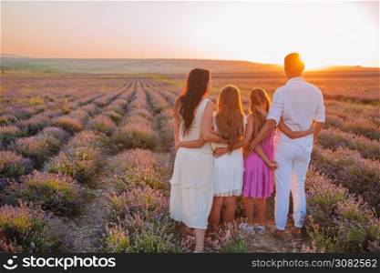 Beautiful young family having fun on purple flower lavender field. Family in lavender flowers field at sunset in white dress and hat