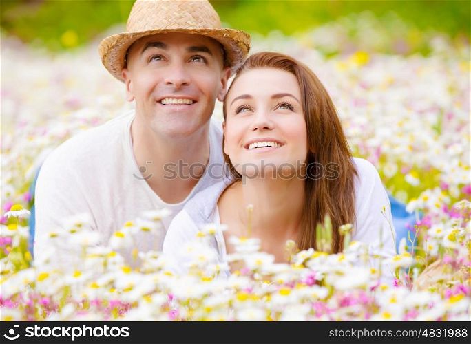 Beautiful young family laying down on wild camomile glade and looking up on sky, having fun in spring park, love concept