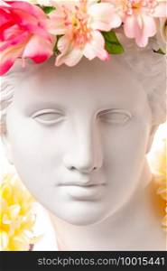 Beautiful young female face and colorful flowers. Plaster antique bust of Venus de Milo in a floral wreath. Beauty spring and summer model girl with fresh bouquet.. Beautiful young female face and colorful flowers. Plaster antique bust of Venus in a floral wreath. Beauty spring and summer model girl with fresh bouquet.