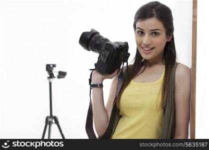 Beautiful young female holding camera against white background