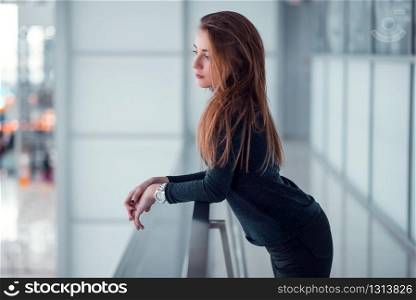 Beautiful young female posing on glazed balcony. Airport at the background.
