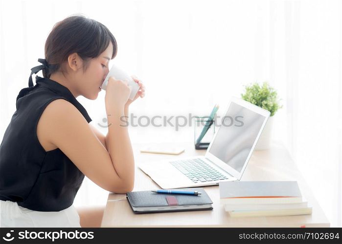 Beautiful young freelance asian woman smiling working and on laptop computer at desk office with professional, girl using notebook and drink coffee, business and lifestyle concept.