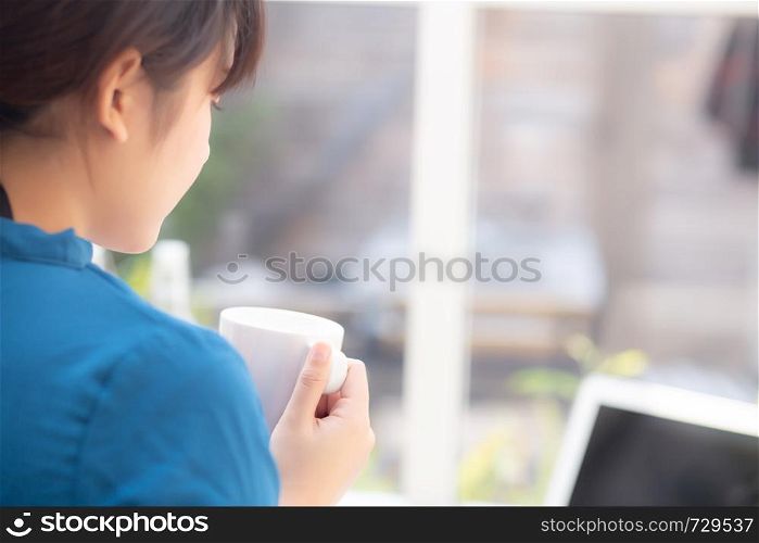 Beautiful young freelance asian woman smiling working and on laptop computer at desk coffee shop with professional, asia girl using notebook and drink coffee, business and lifestyle concept, back view.