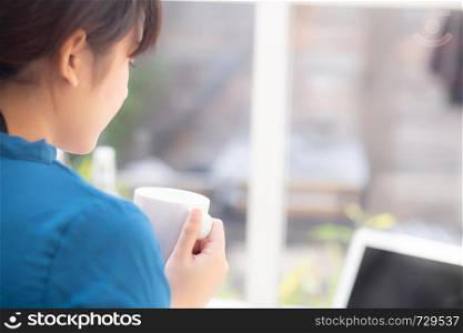 Beautiful young freelance asian woman smiling working and on laptop computer at desk coffee shop with professional, asia girl using notebook and drink coffee, business and lifestyle concept, back view.
