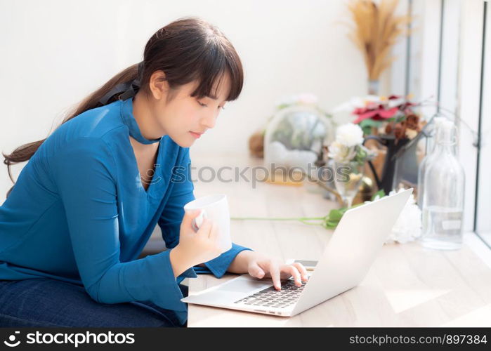 Beautiful young freelance asian woman smiling working and on laptop computer at desk coffee shop with professional, asia girl using notebook and drink coffee, business and lifestyle concept.