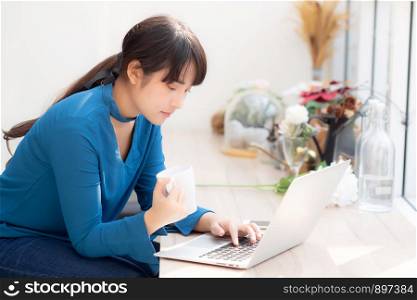 Beautiful young freelance asian woman smiling working and on laptop computer at desk coffee shop with professional, asia girl using notebook and drink coffee, business and lifestyle concept.