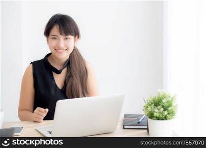 Beautiful young freelance asian woman smiling working and typing on laptop computer at desk office with professional, girl using notebook checking email or social network, business and lifestyle concept.