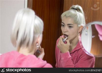 Beautiful young girl applying makeup in bathroom front of mirror.