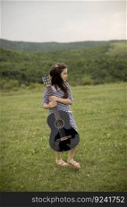 Beautiful young girl carrying her guitar in green nature