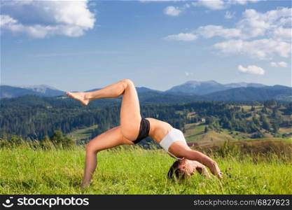 Beautiful young girl doing yoga asana at the summer meadow