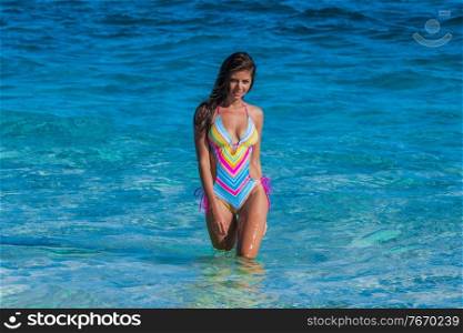 Beautiful young girl in swimsuit walks in transparent sea waves. Girl in swimsuit walks in sea waves