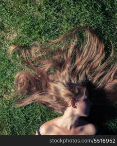 beautiful young girl is lying on green grass in the evening time. The girl lays on a grass of a meadow
