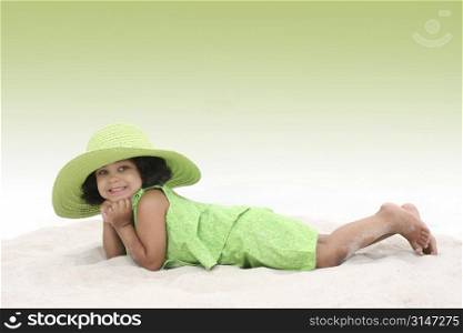 Beautiful Young Girl Laying In the Sand in green summer clothes and big green hat. Beautiful eyes.