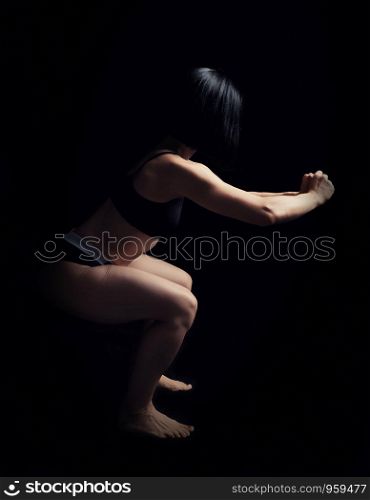 beautiful young girl of athletic appearance with black hair does squats, low key